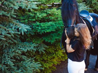 年轻女子站在树旁亲吻马